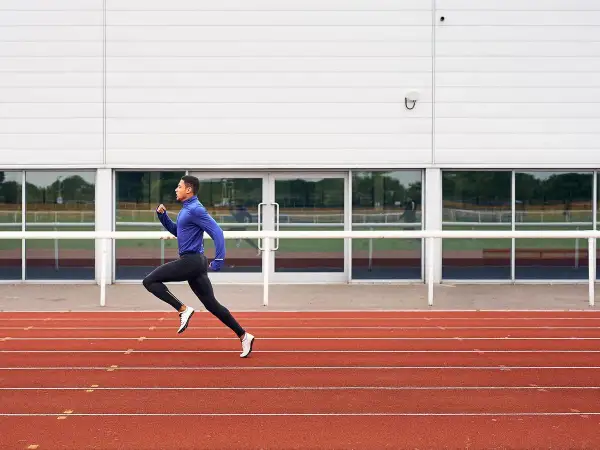Un atleta con ropa deportiva azul y negra corre en una pista de atletismo roja, capturando la esencia de una serie running.