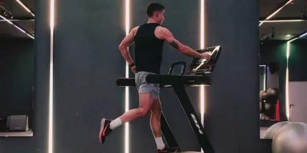 Hombre entrenando en cinta, ajustando la velocidad. El gimnasio moderno con luces LED crea un ambiente dinámico para el ejercicio.