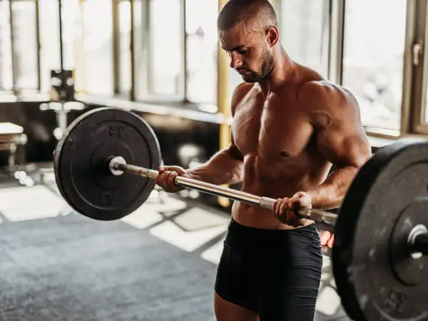 Hombre musculoso levanta barra en gimnasio. Si buscas como engordar de forma saludable, el entrenamiento de fuerza es clave.