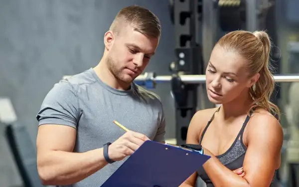 Un personal trainer que es, explica un plan de entrenamiento a una mujer en un gimnasio.