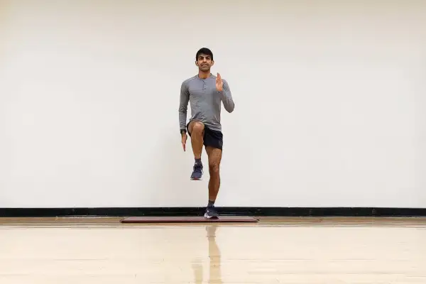 Hombre realizando ejercicio de pliometría para corredores, levantando una rodilla y extendiendo un brazo.