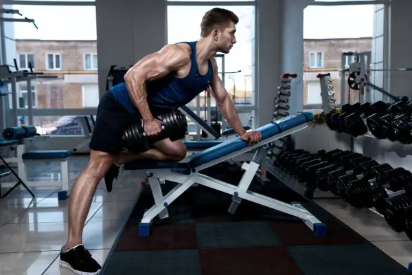 Hombre musculoso haciendo remo inclinado con mancuerna en un gimnasio.