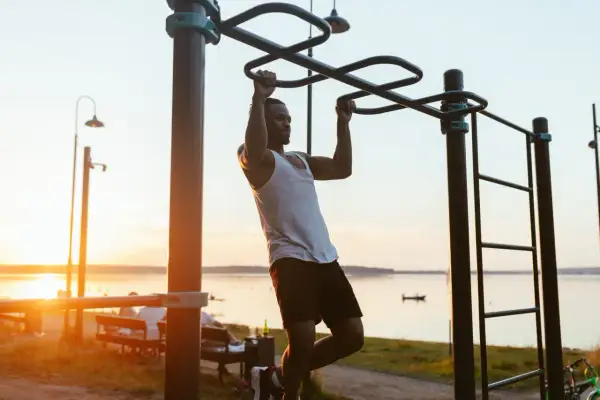 Hombre entrenando en barra exterior, aprendiendo como hacer dominadas al atardecer.