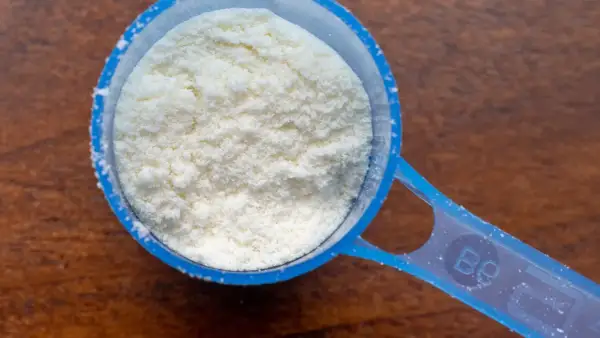 Cuchara dosificadora azul llena de polvo blanco, quizás proteína en polvo. ¿Tomar proteínas es malo?