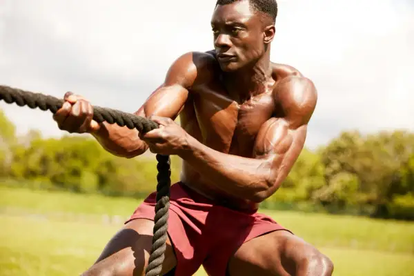 Hombre musculoso en entrenamiento espartano, tirando de una cuerda con fuerza.