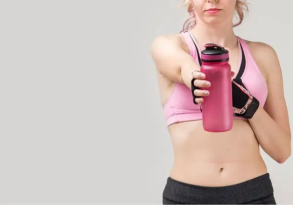 Mujer con ropa deportiva sostiene botella rosa. Guía para como tomar creatina por primera vez.